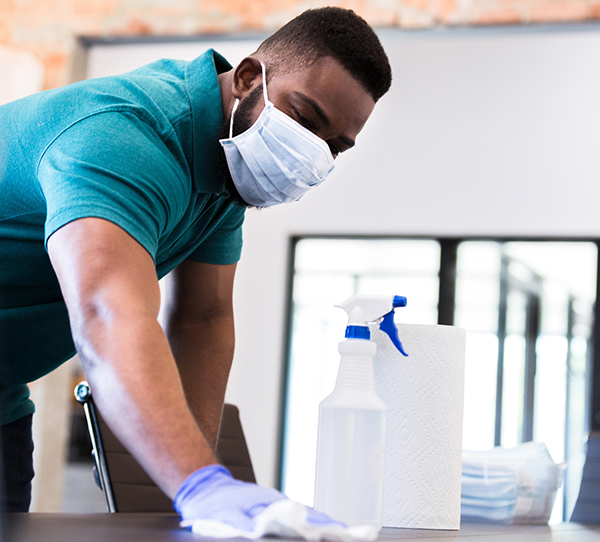 man disinfecting office table wearing mask and gloves